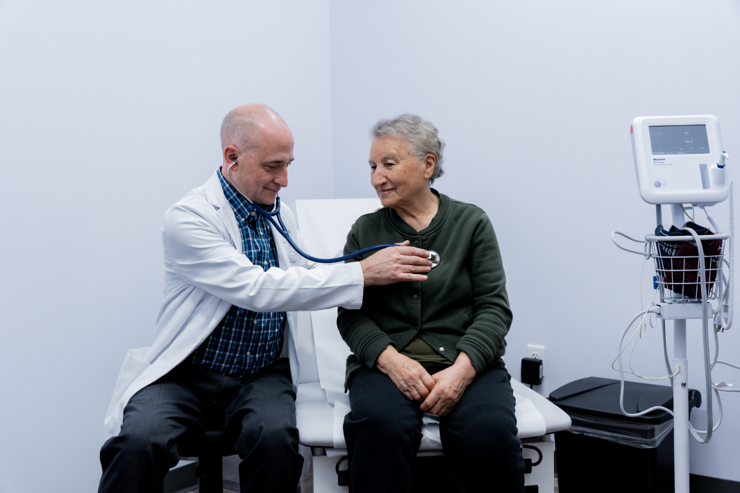 Dr. Brown listening to a female patient's heart in an exam room at ApexMed Primary Care