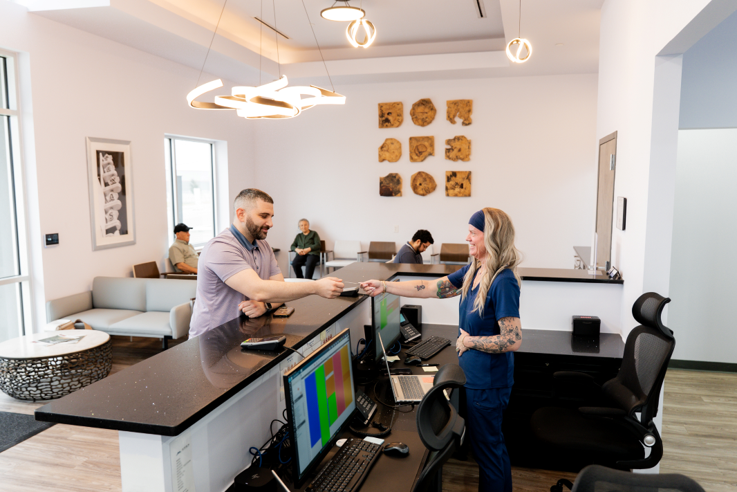 Adult male patient checking in for an appointment at front desk of ApexMed Primary Care with waiting room in the background