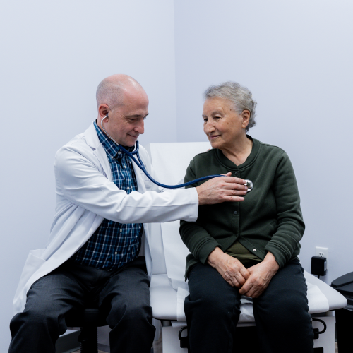 Dr. Brown listening to a female patient's heart in an exam room at ApexMed Primary Care representing ApexMed Primary Care's services